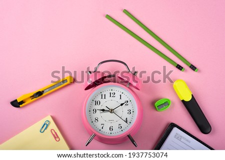 A pink color table clock with a Marker pencils cutter and Sticky note on a pink background.