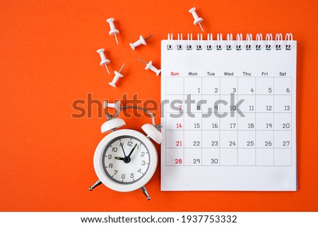 white calendar page , alarm clock and thumbtacks on grunge  orange paper background  Royalty-Free Stock Photo #1937753332
