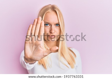 Young blonde girl wearing casual clothes doing stop sing with palm of the hand. warning expression with negative and serious gesture on the face. 