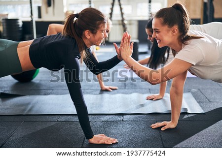 Optimistic young ladies doing plank exercises and high-fiving each other Royalty-Free Stock Photo #1937775424