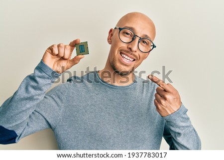 Bald man with beard holding cpu computer processor smiling happy pointing with hand and finger 