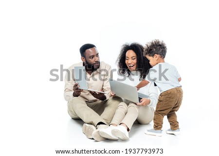 african american boy using laptop together with father and laughing mom on white