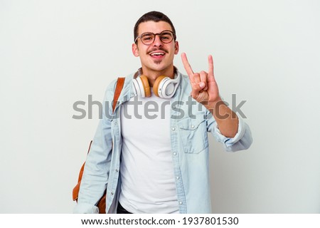 Young caucasian student man listening to music isolated on white background showing a horns gesture as a revolution concept.