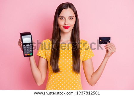 Photo of attractive serious young woman hold card reader debit card wear yellow dotted t-shirt isolated on pink color background