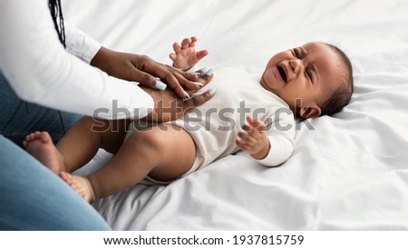 Portrait of black mother doing belly massage for crying baby Royalty-Free Stock Photo #1937815759