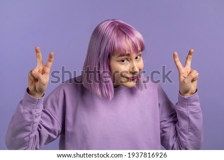 Pretty woman with dyed purple hair showing with hands and two fingers air quotes gesture, bend fingers isolated over violet background. Not funny, irony and sarcasm concept.