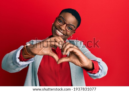 Young african american woman wearing business jacket and glasses smiling in love doing heart symbol shape with hands. romantic concept. 