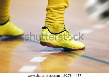 Indoor football player and classic ball. Futsal training for children. Legs of young futsal player in soccer cleats and socks. Indoor sports hall. Player in uniform. Junior level sport background Royalty-Free Stock Photo #1937844457