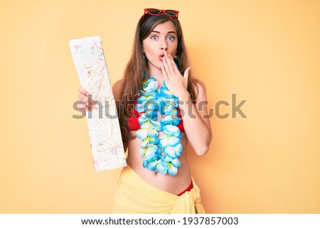 Beautiful young caucasian woman wearing bikini and holding city map covering mouth with hand, shocked and afraid for mistake. surprised expression 