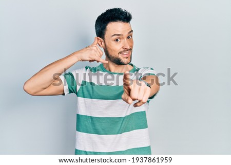 Young hispanic man wearing casual clothes smiling doing talking on the telephone gesture and pointing to you. call me. 
