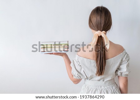 A female student with her back turned holds a stack of books with her hands isolated on a white background. The concept of a student overloaded with learning.