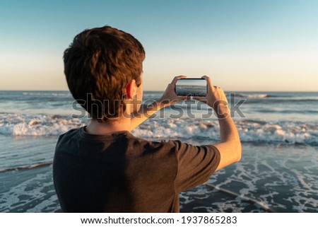 Young man taking a picture of the sea with his smartphone. 