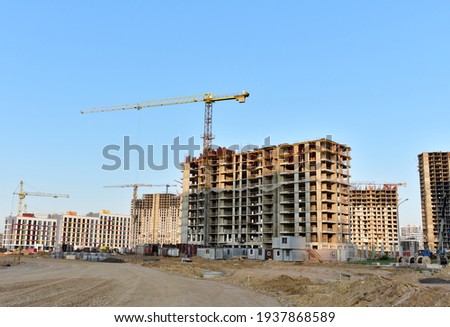 View of a large construction site with buildings under construction and multi-storey residential homes.Tower cranes in action on blue sky background. Housing renovation concept. Crane during formworks Royalty-Free Stock Photo #1937868589