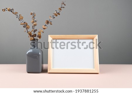 Wooden photo frame with white blank card and vase with dry branches of eucalyptus on table. Mock up poster frame. Stylish template. High quality photo