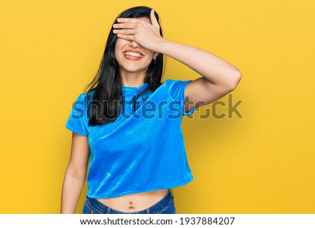 Young hispanic woman wearing casual clothes smiling and laughing with hand on face covering eyes for surprise. blind concept.  Royalty-Free Stock Photo #1937884207