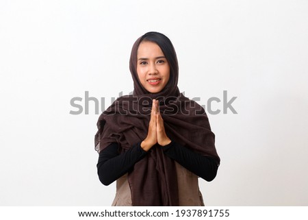 Asian woman in Muslim dress stands up in a greeting pose to Namaste hands, welcoming guests, Eid Fitr greeting. Isolated on white background Royalty-Free Stock Photo #1937891755