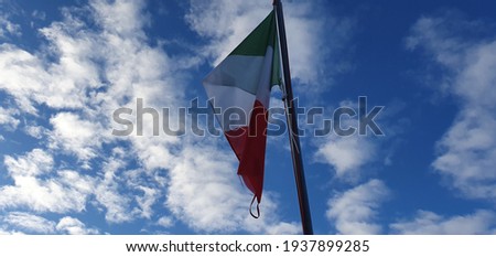 the Italian flag flutters against the light under the blue sky and white clouds