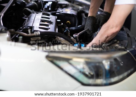Caucasian male mechanic repairs car in garage. Car maintenance and auto service garage concept. Closeup hand and spanner. Royalty-Free Stock Photo #1937901721