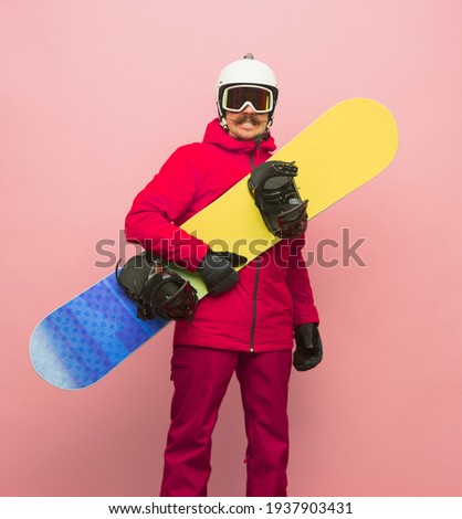Happy man snowboarder with snowboard, ski helmet and gloves in bright pink ski suit posing isolated on pink background. Concept of human emotions, fun, sport and healthy life. Copy space for ad.