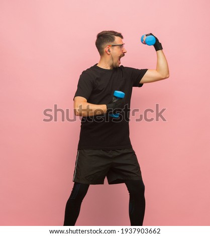 Powerful. Portrait of young Caucasian man in black sports attire with weights isolated over pink background. Concept of human emotions, facial expression, funny meme emotions, sports. Copyspace for ad