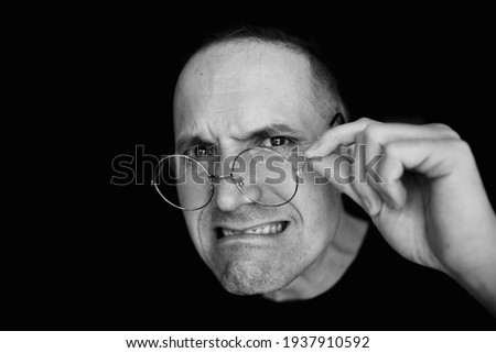 A crazy strange man with his glasses down. Black and white photo. The mouth is twisted. Perplexity. Discontent. Boss, Teacher.. On a black background