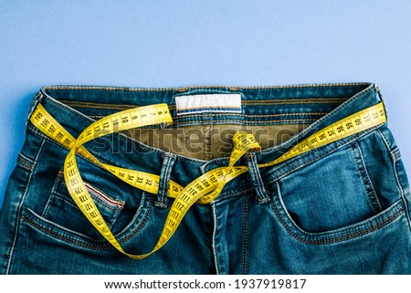 The concept of a healthy lifestyle and diet. Blue jeans with a yellow measuring tape instead of a belt.
