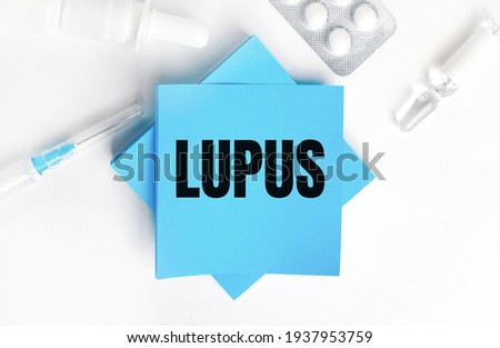 On a white background, a syringe, ampoule, pills, a vial of medicine and light blue stickers with the inscription LUPUS. Medical concept