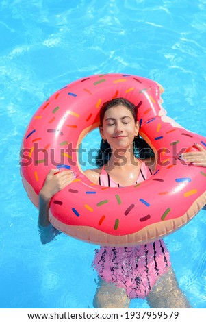 Beautiful young girl on an inflatable ring. Smiling happy girl floats on an inflatable matt circle in the pool.