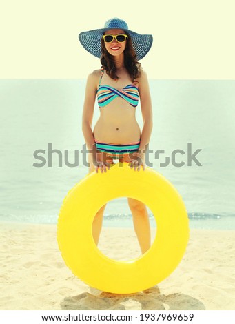 Summer portrait of happy smiling woman with inflatable ring wearing a straw hat on a beach, sea background