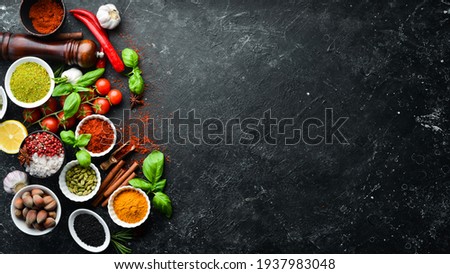 Set of colored spices in bowls and herbs on a black stone background. View from above. Top view.