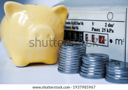 Coins with yellow piggy bank near  the domestic gas meter. Symbolic depiction of energy savings at home, utility bills, smart energy consumption. Toned image, selective focus.