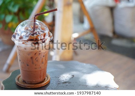 Iced chocolate or cool cocoa drink served on wooden table. Refreshing coffee, cold choco milk with whipped cream on top with natural background in cafe. Royalty-Free Stock Photo #1937987140