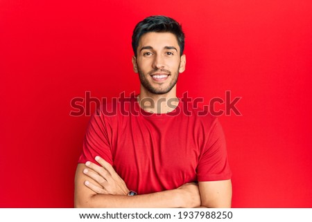 Young handsome man wearing casual tshirt over red background happy face smiling with crossed arms looking at the camera. positive person. 
