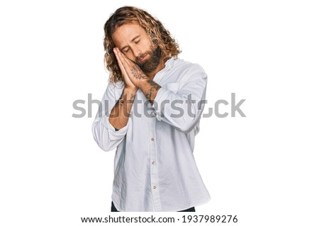 Handsome man with beard and long hair wearing casual clothes sleeping tired dreaming and posing with hands together while smiling with closed eyes. 