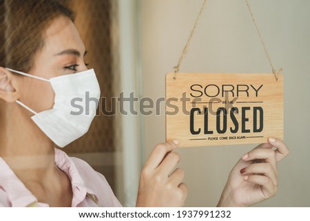 Hand of young asian owner coffee shop woman turning sign board to closed with wearing face mask, protection to pandemic of coronavirus.Close store, restaurant due to lockdown, quarantine of covid.