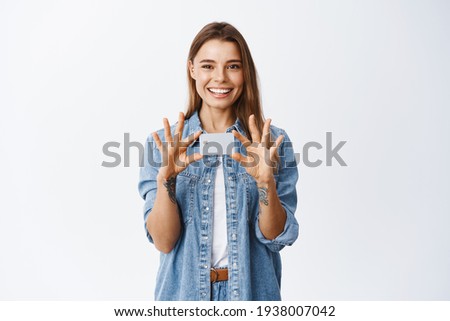 Image of young smiling caucasian woman with positive emotion, showing plastic credit card over chest, recommend bank deposit, standing over white background