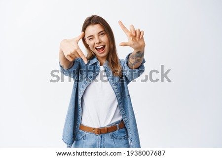 Portrait of beautiful cool girl picturing moment, showing hand camera frames and winking, checking out something awesome, standing over white background
