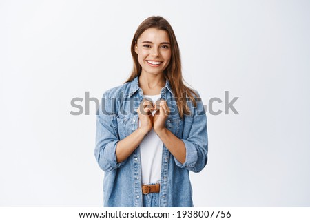 Beautiful romantic girl showing heart gesture, I love you sign, smiling happy at camera, standing against white background