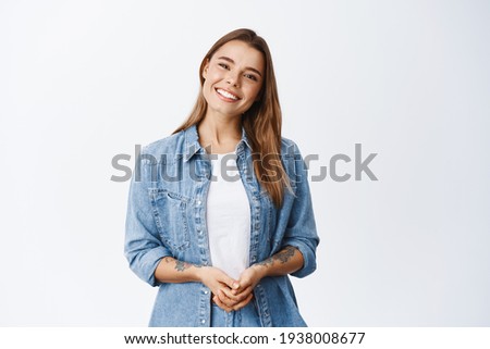 Beautiful smiling woman looking friendly and ready to help customer or client, holding hands together and staring at camera, white background