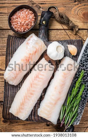 Fresh Raw cod loin fillet steaks on wooden board with butcher knife. wooden background. Top view