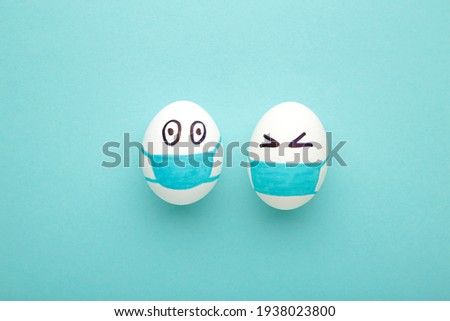 White Easter eggs in protective medical mask on blue background. Easter on quarantine concept with place for text. Stop VIRUS COVID-19. Copy space. Egg in mask. Top view