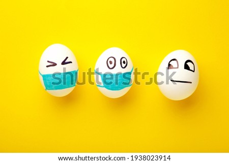 White Easter eggs in protective medical mask and one egg without mask on yellow background. Easter on quarantine concept with place for text. Stop VIRUS COVID-19. Copy space.