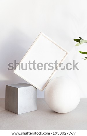 Mock-up poster frames in the interior of geometric shapes. Modern still life scene in neutral colors with an olive branch. Minimal composition with white photo frame and interesting shadows
