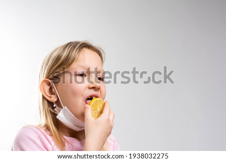 Beautiful smiling little girl with a lemon isolated on white background. Girl's Reaction to a Slice of very Sour Lemon with face mask.