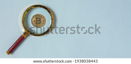 Bitcoin coin through magnify glass on blue background. banner with copy space