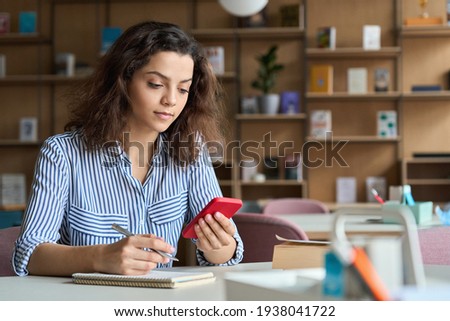 Hispanic latin young teen girl college student holding smartphone studying on cell, distance learning using apps for education, elearning on mobile phone in university campus or creative office. Royalty-Free Stock Photo #1938041722