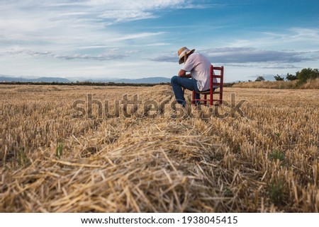Farmer with straw hat and hoe sitting on a red chair in the middle of the field. Agriculture concept. Royalty-Free Stock Photo #1938045415