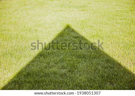 Shadow in the shape of triangle on the green lawn. Nature photo backgrounds. 