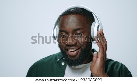 Portrait of positive afro man listening music on earphones indoors. Closeup african american dj enjoying music in headphones on grey background. Smiling african guy posing in studio.