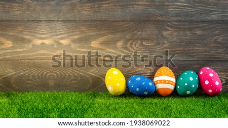 Happy Easter background. Easter eggs on green grass on wooden background. Festive Easter banner with painted colorfull eggs. Copy space
